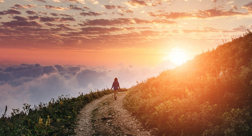 woman hiking on trail around mountian toward sunset