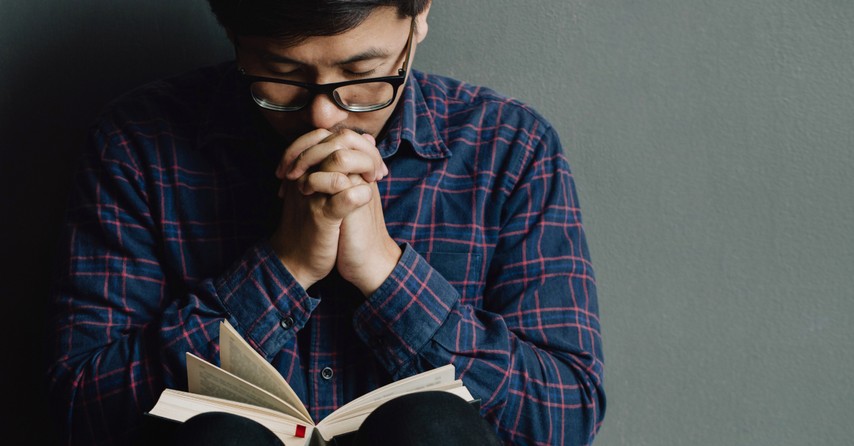 man eyes closed praying with Bible open on lap