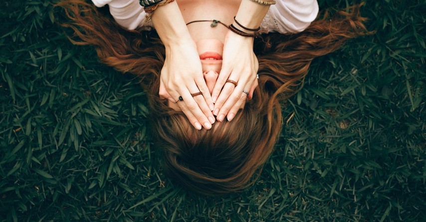 woman with hands over eyes laying on ground, why do i feel so inadequate?