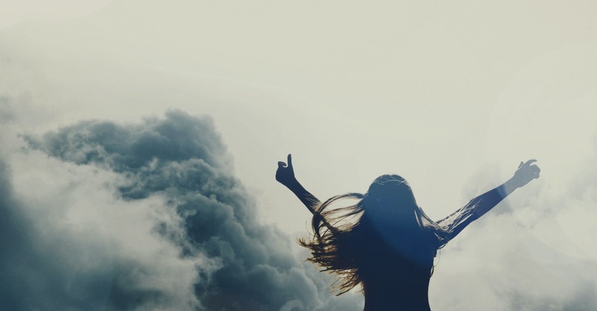 woman with arms raised with clouds behind