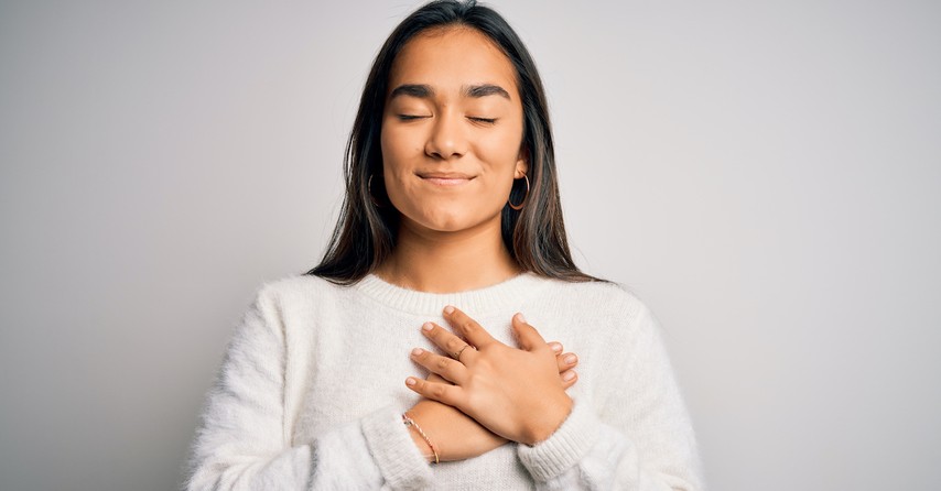 thankful and grateful woman smiling with eyes closed and prayer hands over heart, thanks be to God