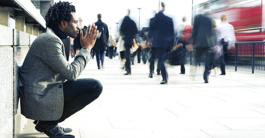 man pondering about life sitting on sidewalk as people rush by