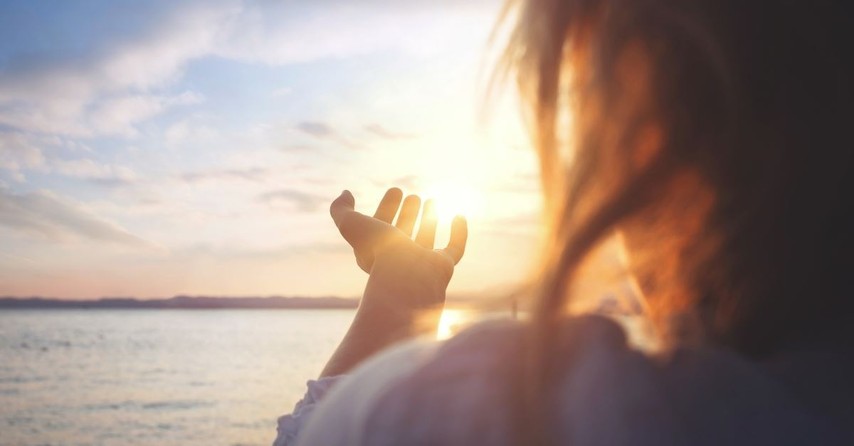 woman holding out her hand with sunrise background