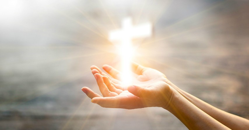 woman's hands holding glowing cross