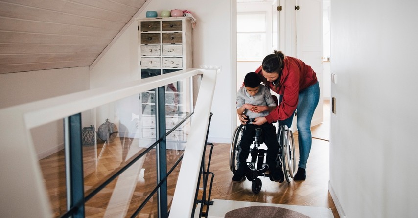 Mom fastening a seatbelt on her son in a wheelchair