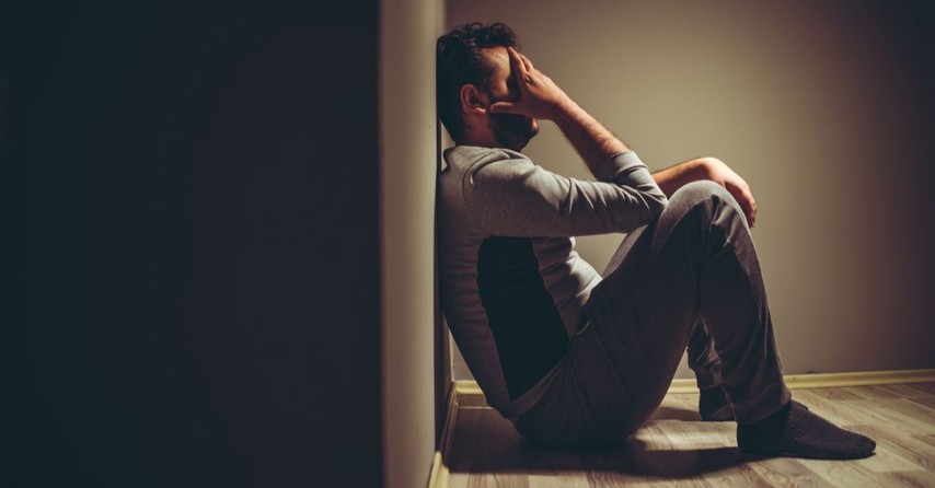 Depressed, sad man sitting on the floor against a wall