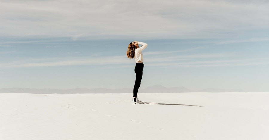 woman standing in white sand desert alone looking up