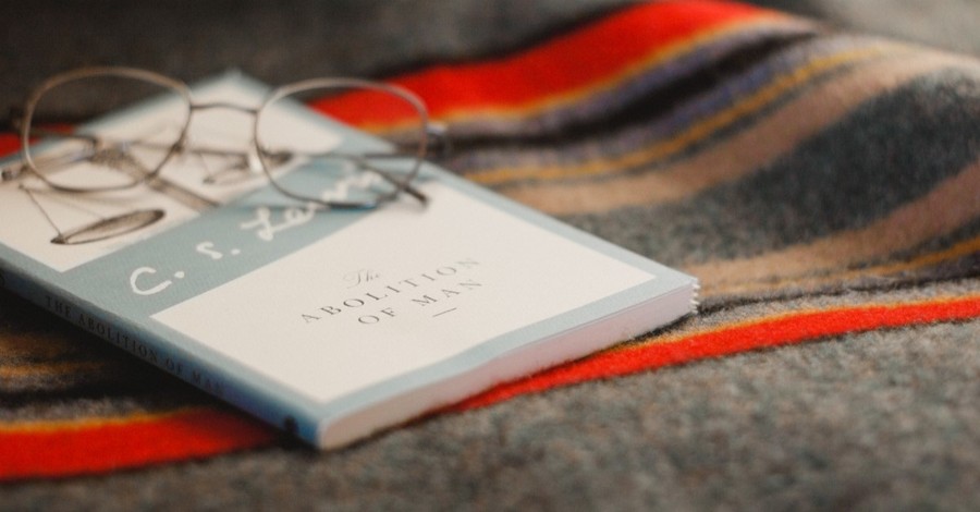 CS Lewis book The Abolition of Man with eyeglasses on top of it lying on blanket