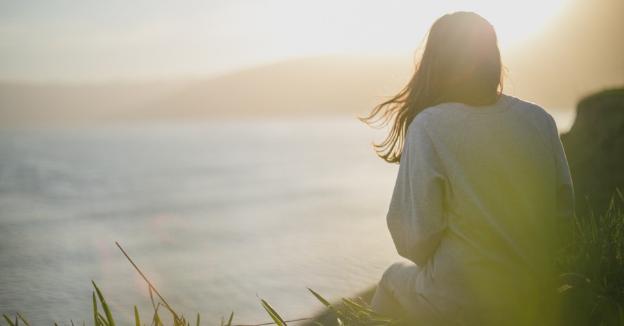 Back view of a woman sitting by the ocean