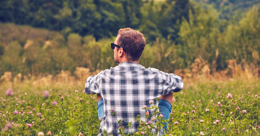 back view of many with sunglasses sitting in grass in meadow