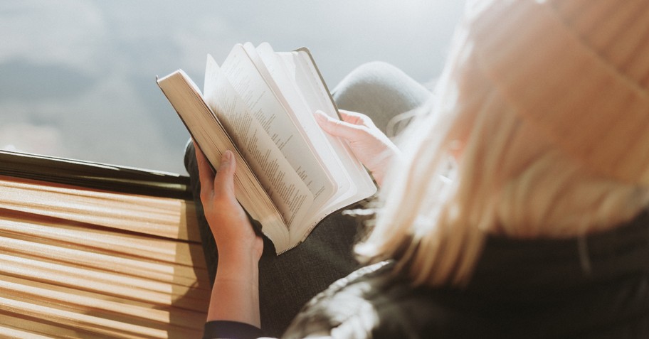 back view of young woman reading Bible outdoors