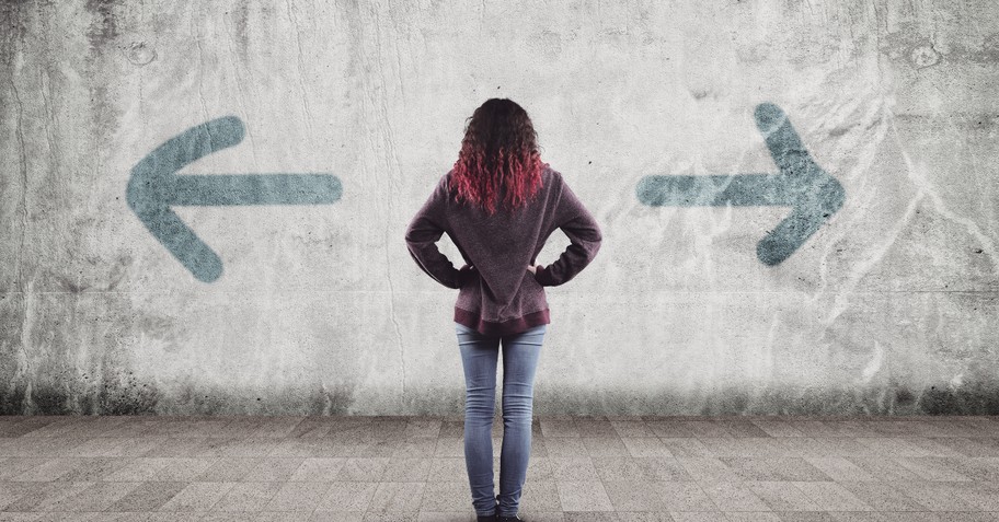 back view of young woman looking at arrows pointing in opposite directions