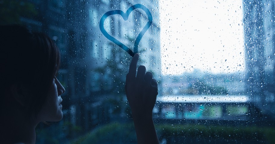 woman tracing heart on window on rainy day