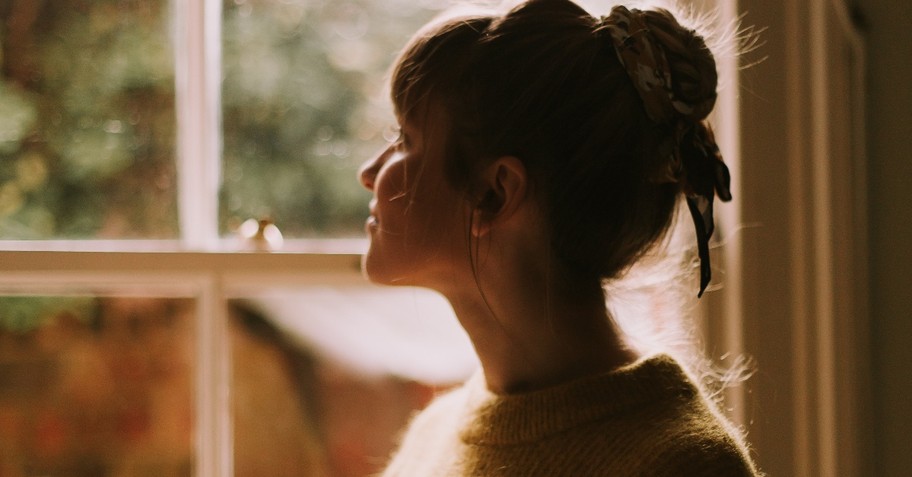 woman in sweater looking out window, spiritually asleep