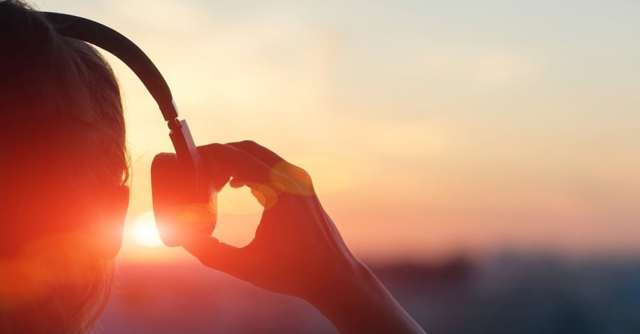 Woman lifting her headphones while listening to music at sunset