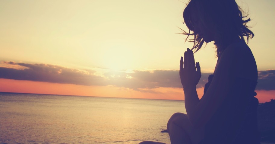 Woman praying on a rock with the view of the sea