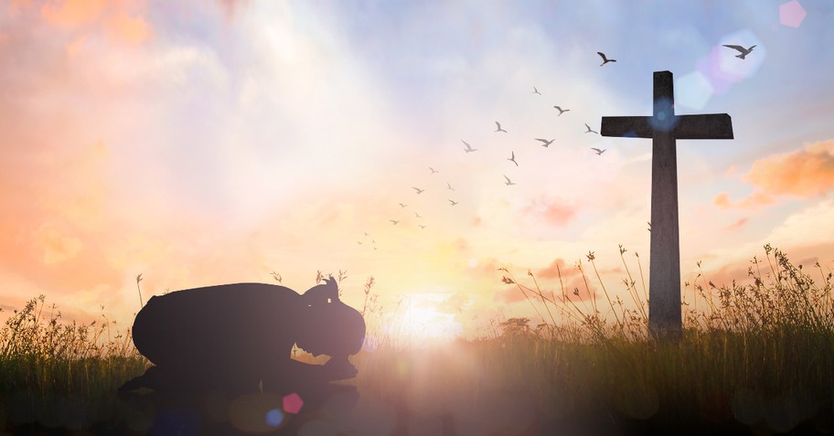 woman kneeling before the cross at sunset