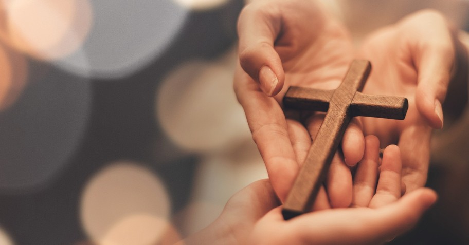 Hand holding a cross forming a heart shape