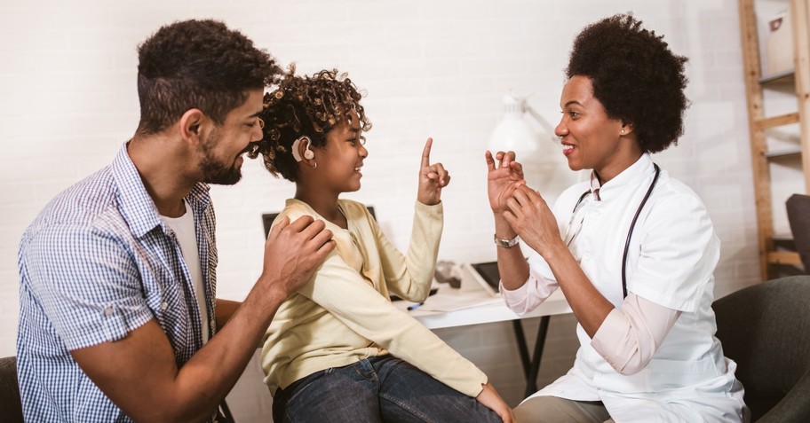 Girl with a hearing aid signing with doctor