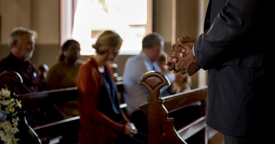 Pastor standing in front of the congregation, with hands clasped