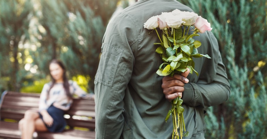 Man holding flowers behind his back to surprise a woman