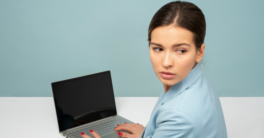 A woman on a computer looking over her shoulder, secretive