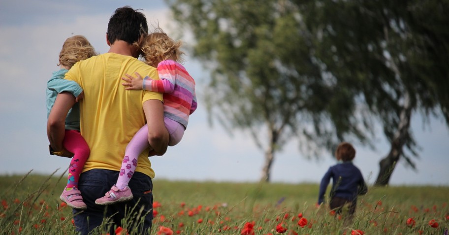 dad carrying two toddlers with one running ahead outdoors in nature