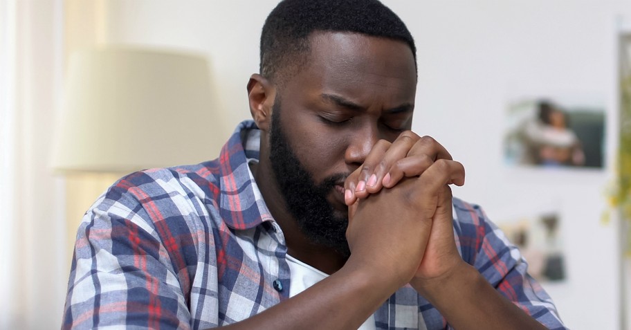 A man with eyes closed and hands folded in prayer