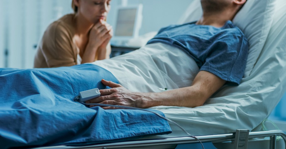 Woman praying over a sick man at the hospital, anointing oil