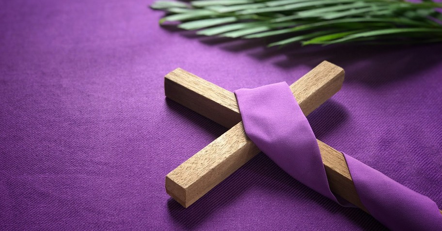 Cross with a purple sash on it, with green palm branches nearby