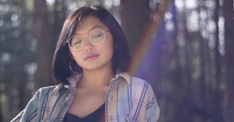 woman sitting outside with eyes closed and rainbow reflection behind her