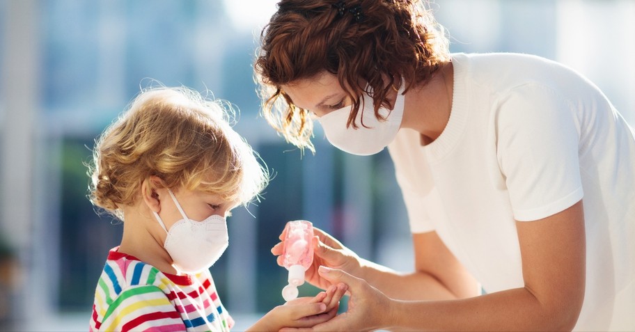 mom wearing face mask for COVID-19 putting hand sanitizer on child's hands