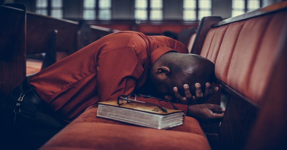 man in orange shirt praying in church pews, in the world but not of it