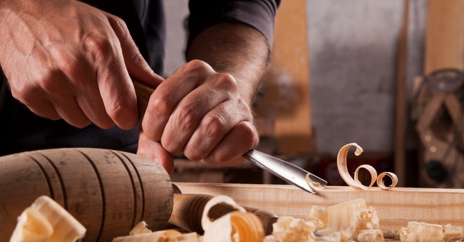 Man's hands carving wood with chisel