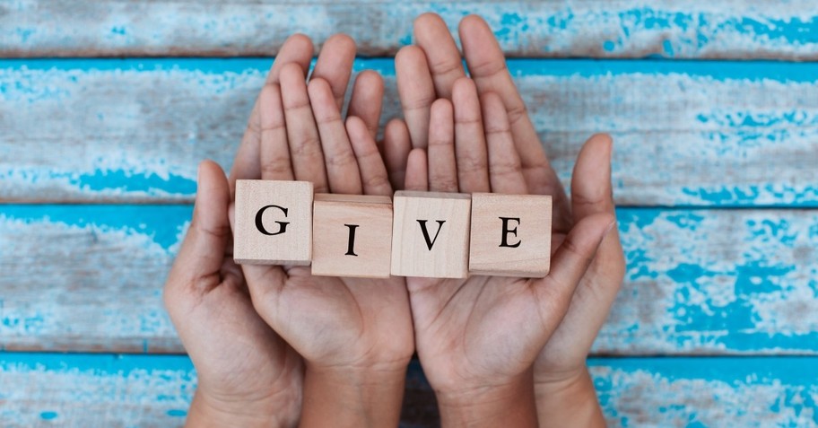 Alphabet letter wooden blocks with words GIVE in child and parents hands, social gospel