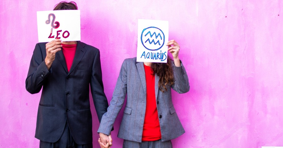 Man and woman holding hands and holding up their astrology signs