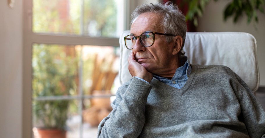 a senior man looking sadly out a window