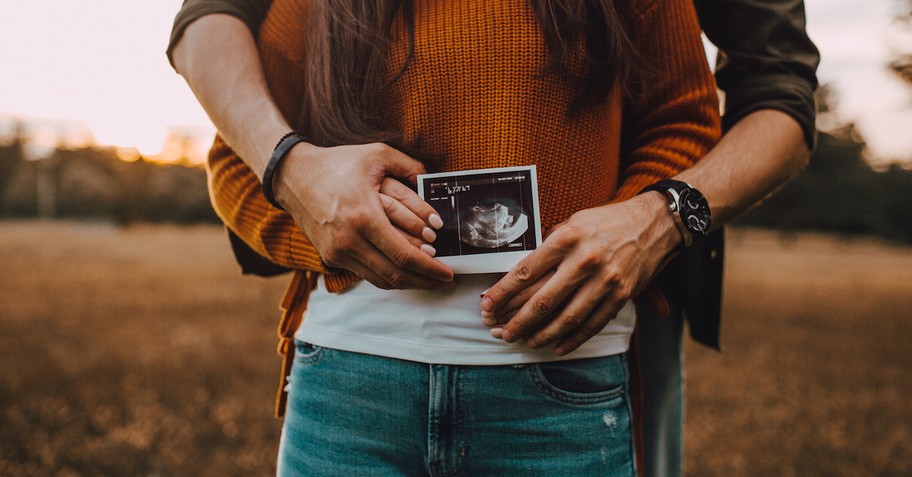 A couple standing with arms around each other, holding a sonogram picture