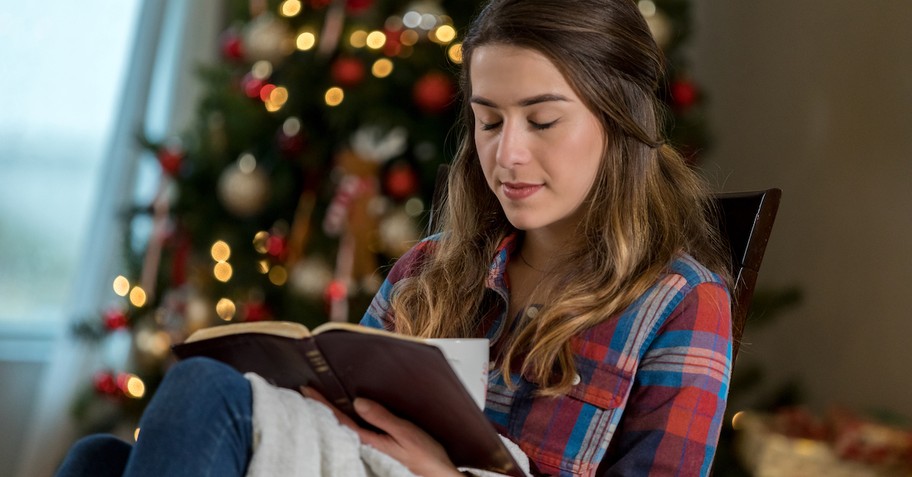 Woman reading Bible by Christmas Tree