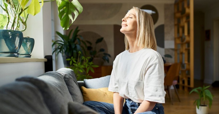 A calm, peaceful woman sitting by a window, smiling up at the sunlight