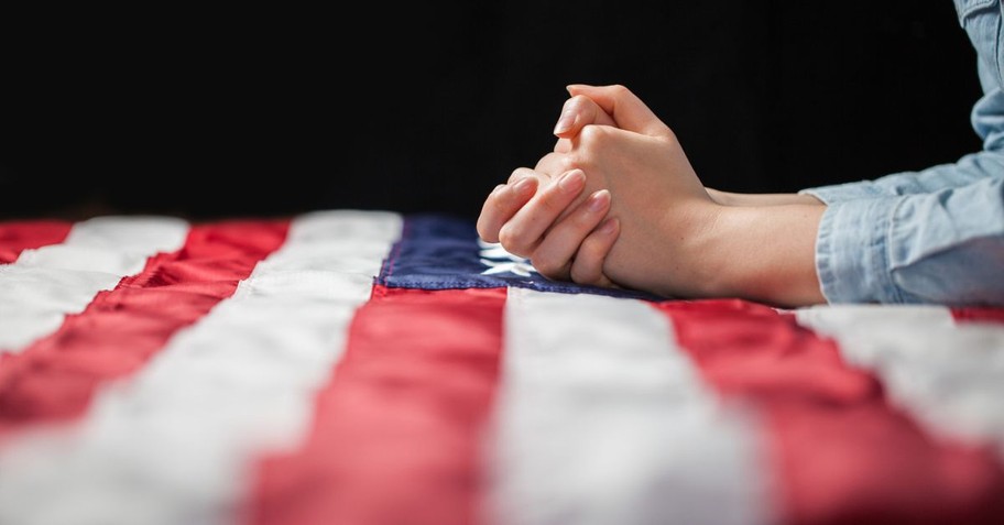 A person with hands folded in prayer atop an American flag