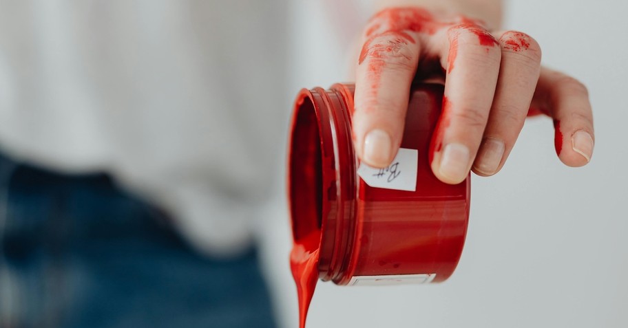hand holding red paint pouring from small container