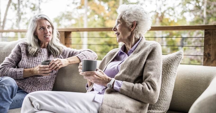 Senior old woman and adult daughter mentor talking on couch with coffee porch