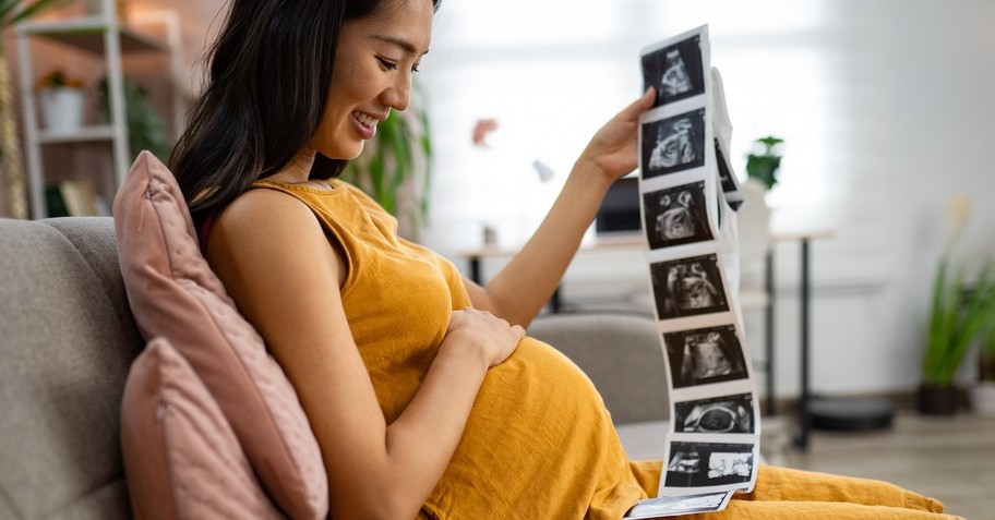 Pregnant mom with ultrasound baby bump sitting on couch pregnancy