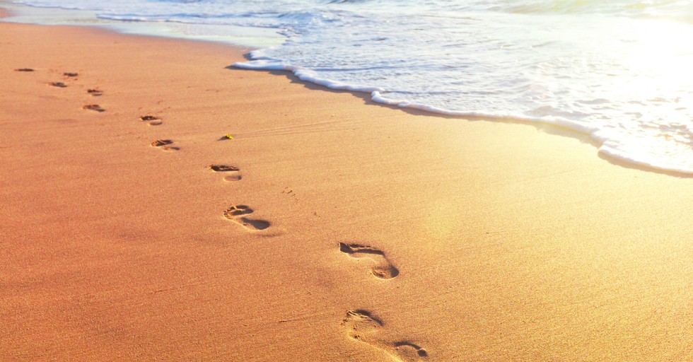 footprints in sand along surf edge