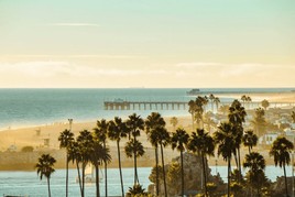A scenic view of Orange County, California, featuring the coastline, palm trees, and a vibrant sunset over Huntington Beach, capturing the region’s lively atmosphere.